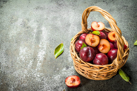 Fresh plums in a basket with leaves. On a rustic background.の写真素材