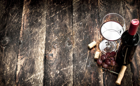 Red wine with a branch of grapes and a corkscrew. On a wooden background.の写真素材