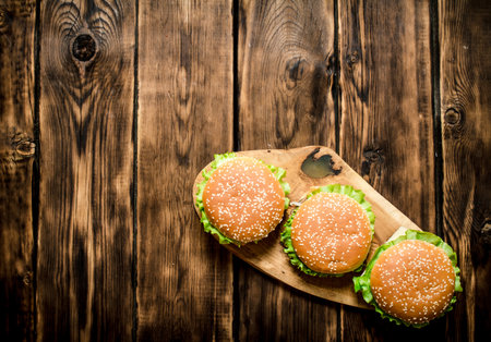 Three finished Burger with meat and vegetables on wooden stand. On wooden background. Top view.の写真素材