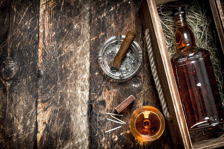 Cognac background. A bottle of cognac in a box with a glass and a cigar. On a wooden background.の写真素材