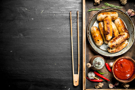 Sausages in a frying pan with sauce on a wooden tray. On the black chalkboard.の写真素材