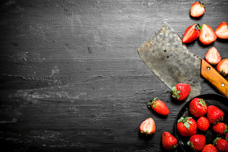 Sliced strawberries with the old hatchet. On the black wooden table.の写真素材