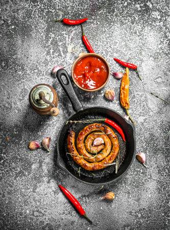 Sausage in a frying pan with hot peppers, garlic and sauce. On a rustic background.の写真素材