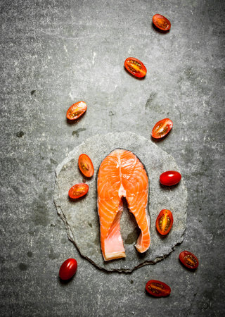 piece of raw trout and tomatoes. On a stone background.の写真素材