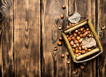 Hazelnuts in a basket with dry leaves. On wooden background.の写真素材