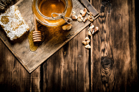 Honey background. Sweet honey in the comb, glass jar with nuts. On wooden background.の写真素材