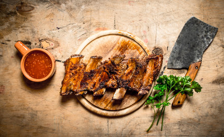 Barbecued ribs with tomato sauce and a carving hatchet. On wooden background.の写真素材