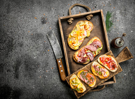 Various sandwiches with seafood, meat and vegetables on an old tray. On a rustic background.の写真素材