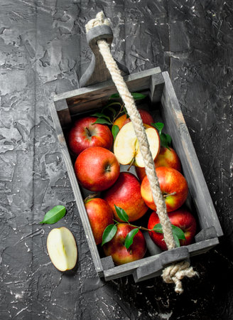 Red apples with leaves and Apple slices in a wooden box. On a dark wooden background.の写真素材