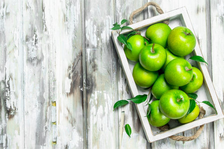 Green juicy whole apples in a wooden box. On a white wooden background.の写真素材