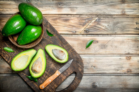 Avocado in a bowl on a black chopping Board with a knife. On a wooden background.の写真素材