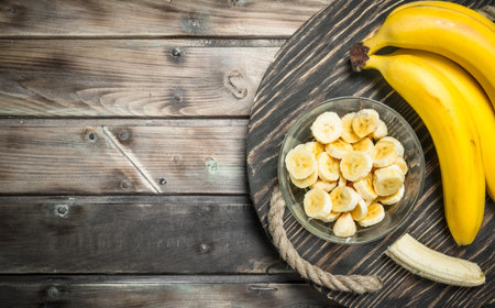 Bananas and banana slices in a glass bowl on the old dressing. On a black wooden background.の写真素材