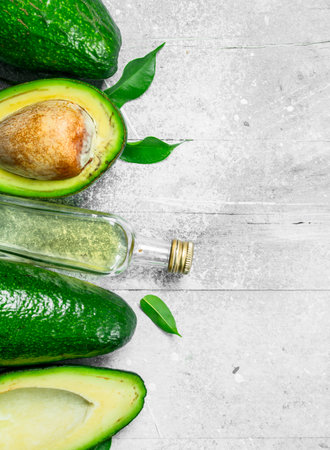 Avocado oil and avocado with leaves. On white rustic background.の写真素材