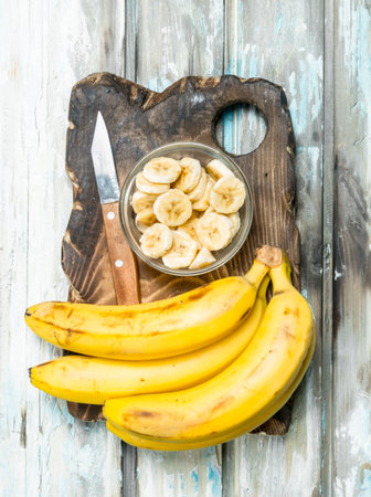 Bananas and banana slices in a glass bowl on an old cutting Board. On a white wooden background.の写真素材