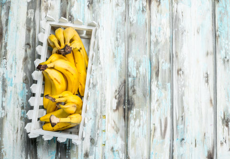 Fresh bananas in a white plastic basket. On a white wooden background.の写真素材