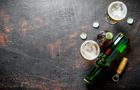 Beer in glasses and bottles with opener and covers. On rustic backgroundの写真素材