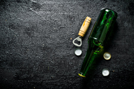 Beer in a glass bottle with opener and covers. On black rustic backgroundの写真素材