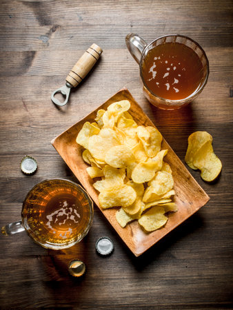 Beer in glass mugs and chips on a plate. On wooden backgroundの写真素材