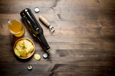 Beer in a bottle and a glass with chips and opener. On wooden backgroundの写真素材
