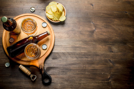 Beer in bottles and glasses on the cutting Board and chips in the bowl. On wooden backgroundの写真素材