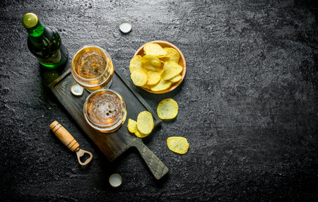 Beer in glasses on the cutting Board and chips in the bowl. On black rustic backgroundの写真素材