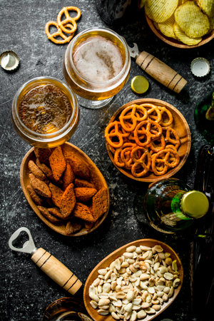 Beer and an assortment of different snacks with openers. On black rustic backgroundの写真素材