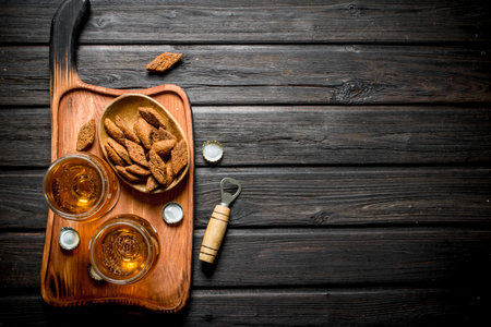 Beer in glasses and crumbs in bowl on cutting Board. On black wooden backgroundの写真素材