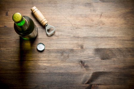 One bottle of beer with opener. On wooden backgroundの写真素材