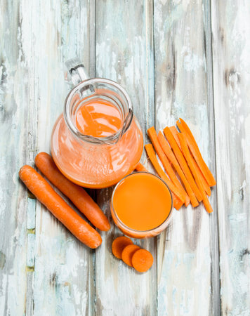 Carrot juice in the jug. On wooden backgroundの写真素材