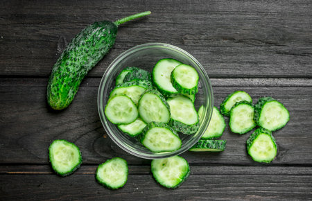 Sliced cucumbers in a glass bowl. On black wooden backgroundの写真素材