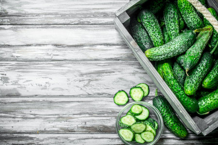 Cucumbers in the box and cucumber slices in the bowl. On wooden backgroundの写真素材