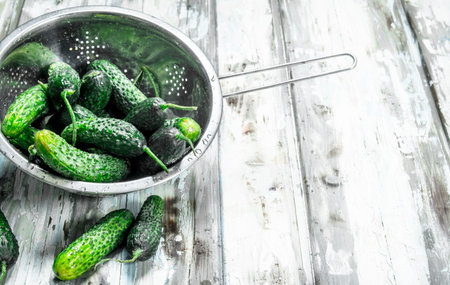Fresh cucumbers in the colander. On white wooden backgroundの写真素材