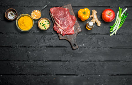 Health food. Raw beef steaks with organic vegetables and spices. On a black rustic background.の写真素材