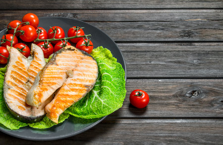 Grilled salmon steaks with tomatoes on a plate. On a wooden background.の写真素材