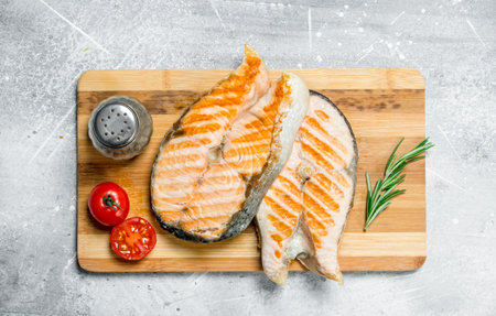 Grilled salmon steaks with tomatoes and a sprig of rosemary. On a rustic background.の写真素材