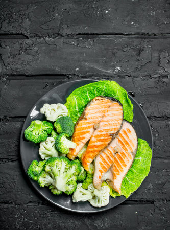 Grilled salmon steaks with fresh broccoli in a plate. On black rustic background.の写真素材