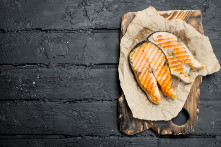 Grilled salmon steaks on old paper. On black rustic background.の写真素材