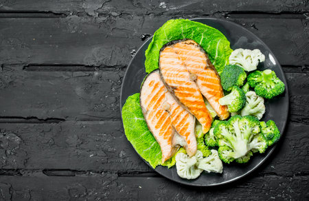 Grilled salmon steaks with fresh broccoli in a plate. On black rustic background.の写真素材