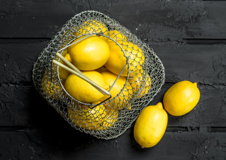 Fresh lemons in the iron basket. On rustic backgroundの写真素材