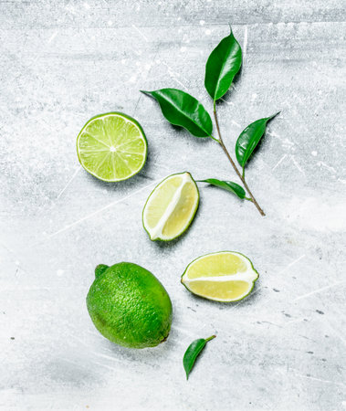 Pieces of fresh juicy lime with foliage. On white rustic backgroundの写真素材