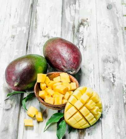 The mango pieces in a bowl and a whole mango. On wooden backgroundの写真素材