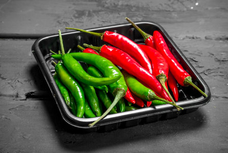 Hot fresh pepper on tray. On black rustic backgroundの写真素材