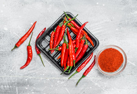 Ground red pepper in a bowl and the peppers on the tray. On rustic backgroundの写真素材