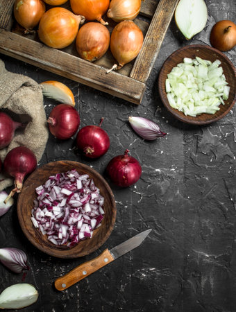 Pieces of onions in a bowl with a yellow onion on tray and red onion in a sack. On rustic backgroundの写真素材