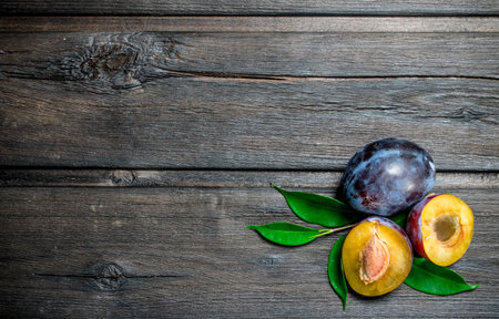 Pieces of ripe plum with leaves. On wooden backgroundの写真素材