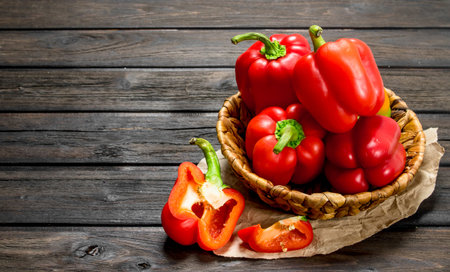 Ripe red sweet peppers in a basket on paper. On wooden backgroundの写真素材