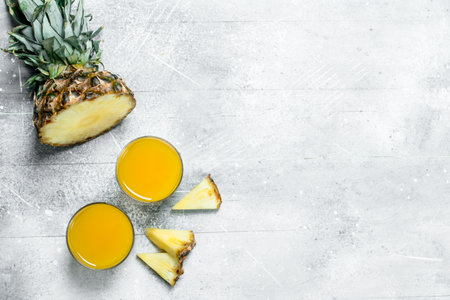 Pineapple juice in a glass and slices of ripe pineapple. On white rustic backgroundの写真素材