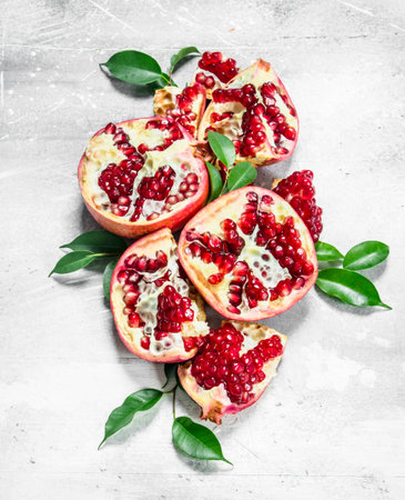 Pieces of ripe pomegranate with leaves. On white rustic backgroundの写真素材