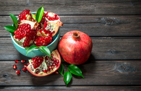 Pieces of ripe pomegranate in bowl and one ripe pomegranate with leaves. On wooden backgroundの写真素材