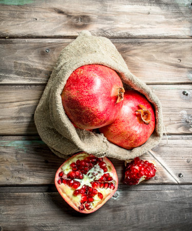 Pomegranates in the sack and half of a fresh pomegranate. On wooden backgroundの写真素材